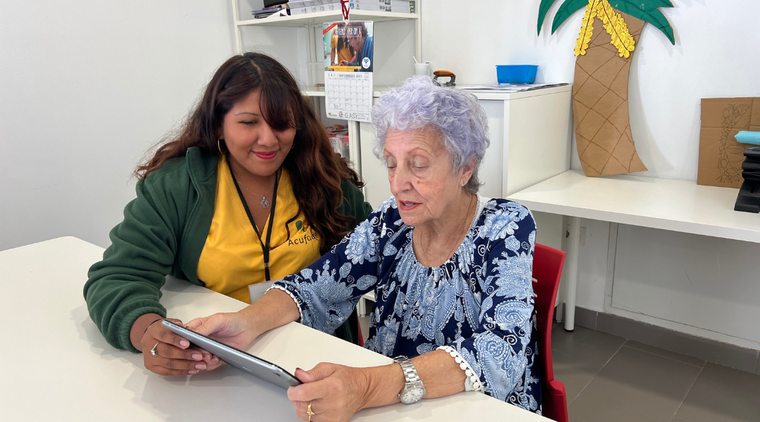 Unidad de Estimulación Cognitiva Una trabajadora de una residencia ayuda a una mujer mayor a usar una tableta.